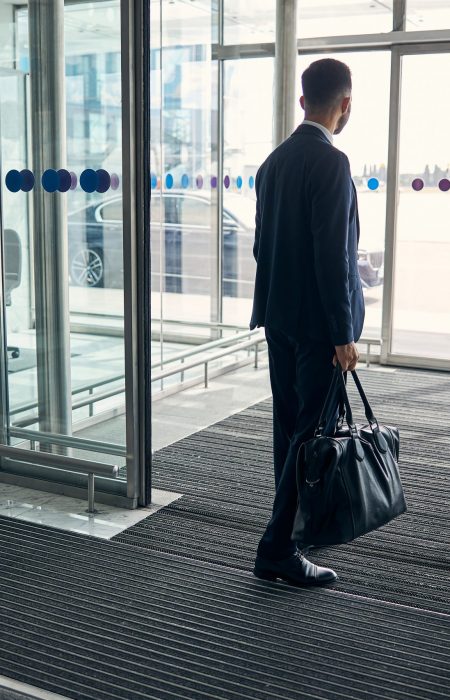 Businessman in a suit walking through entrance hall with a leather suitcase in his hand